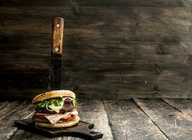 snabb mat. en färsk burger tillverkad från nötkött och grönsaker med en stor kniv. foto
