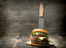 snabb mat. en färsk burger tillverkad från nötkött och grönsaker med en stor kniv. foto