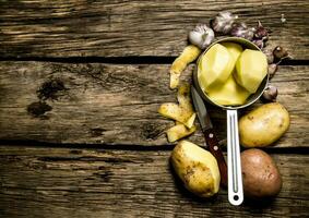 de skalad potatisar i en kastrull med vitlök och kniv på trä- bakgrund . fri Plats för text. foto