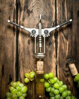 vit vin med en korkskruv och grenar av vindruvor. foto