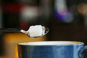 häller vit socker kub i en kaffe kopp foto