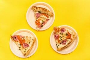 hämtmat och leverans. tre bitar av pizza i disponibel plast plattor på en gul bakgrund. lunch för en grupp av vänner foto