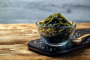 alger laminaria kelp i en glas skål strö sesam på en trä- styrelse. tång sallad. asiatisk mat foto