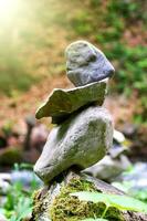 sten pyramid, sten balansering konst. närbild av en stack av stenar i perfekt balans i en berg skog. Sol strålar. meditation, balans, fred. hobby. vertikal Foto. foto