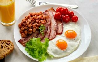 hjärtlig frukost med krypterade ägg, bacon, bönor, körsbär tomater, hemlagad bröd, orange juice på en betong bänkskiva. engelsk frukost begrepp. foto