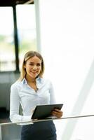 ung kvinna med digital läsplatta stående i de modern kontor hall foto