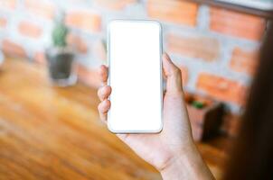 ung kvinna innehav smart telefon med tom skärm medan Sammanträde på de levande rum foto