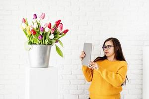 kvinna bloggare håller digital tablett tar bild av tulpaner blommor foto