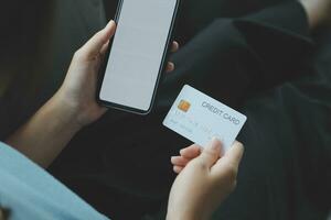 en kreditera kort i de händer av en ung affärskvinna betalar för en företag på en mobil telefon och på en skrivbord med en bärbar dator. foto