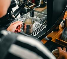 hand av en Barista i de kaffe affär framställning och använder sig av en kaffe maskin till ånga mjölk för en kaffe meny. foto