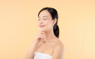 skön flicka asiatisk modell rörande färsk lysande hydratiserad ansiktsbehandling hud på beige bakgrund närbild. skönhet ansikte ung kvinna med naturlig smink och friska hud porträtt. hud vård begrepp foto