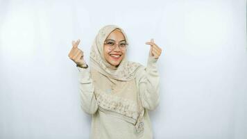 skön leende asiatisk kvinna i traditionell muslim klänning som visar koreanska hjärta med två fingrar korsade, uttrycka glädje och positivitet isolerat över vit bakgrund foto
