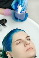 närbild se av frisör pressar schampo från rör in i huvud av kvinna med blå hår medan tvättning hår i särskild handfat foto