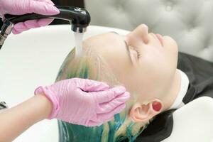 frisör tvättar klientens huvud med grön hår Färg. hårstylist tvättning hår med schampo av kvinna i handfat med dusch i skönhet salong foto