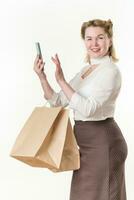 Lycklig kvinna innehar handla påsar och använder sig av mobil telefon app köpa kläder uppkopplad i e-handel Lagra foto