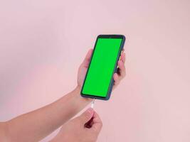 kvinna händer plugging hörlur in i smart telefon med grön skärm isolerat på rosa bakgrund. närbild av hand plugging i hörlurar enhet i smartphone. foto