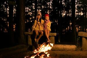 söt liten systrar värma nära lägereld utomhus i kall väder. barn har roligt på läger brand. camping med barn i vinter- tall skog. Lycklig familj på semester i natur. foto