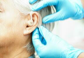 läkare Installera hörsel hjälpa på senior patient öra till minska hörsel förlust problem. foto
