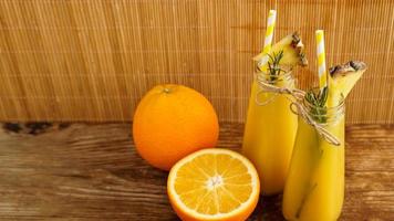 två flaskor tropisk juice med papper sugrör. apelsiner och ananas foto