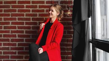 affärskvinna glatt leende bär röd jacka över kontors tegelvägg