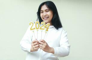 glad ung kvinna asiatisk företag kvinna leende till kamera förbi som visar gyllene glittrade 2024 ljus för 2024 ny år nedräkning firande bär formell vit skjorta isolerat foto