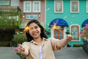 Lycklig ung asiatisk kvinna innehav sparkler fira ny år eve i årgång hus gård, utomhus- trädgård foto