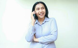 leende asiatisk ung företag kvinna upphetsad till göra en ring upp till talande på cell telefon ser bort med vikta ärm ha på sig formell skjorta isolerat på vit bakgrund foto