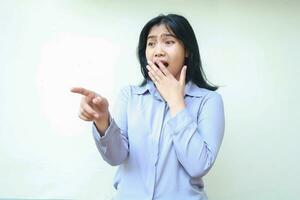 rädd asiatisk ung företag kvinna pekande ser bort chockade beläggning henne mun bred öppen ha på sig formell skjorta stående över isolerad vit bakgrund foto