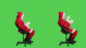 karaktär läser ny berättelse bok verkande tycka om helgon nick i känd röd kostym Sammanträde på stol, grönskärm bakgrund. ung man porträtterar far jul läsning litteratur eller poesi, klok person. foto