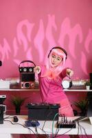 musikalisk konstnär stående på dj tabell blandning techno låt med elektronisk använder sig av mixer trösta, utför musik i främre av folkmassan. asiatisk aerformer med rosa hår njuter till prestera på natt i klubb foto