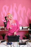 konstnär med rosa hår stående på dj tabell utför elektronisk låt använder sig av professionell skivspelare njuter spelar musik under natt tid i klubb. perfomer håller på med prestanda med audio Utrustning foto