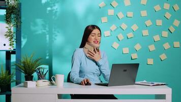 skadade kvinna bär cervical krage kasta kämpar medan arbetssätt på bärbar dator i kontor. sårad anställd med nacke spänna varelse i smärta på färgrik arbetsplats skrivbord över blå studio bakgrund foto