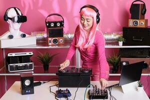 musikalisk konstnär med rosa hår spelar techno låt på professionell mixer trösta, njuter utför musik i klubb under natt tid. asiatisk artist blandning ljud i studio med isolerat bakgrund foto