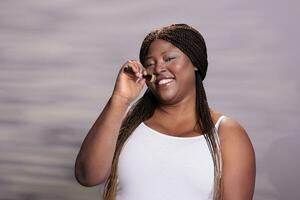 afrikansk amerikan kvinna använder sig av göra upp borsta som mikrofon porträtt. leende ung plus storlek modell sång i smink applicering verktyg, skrattande och har roligt, ser på kamera foto
