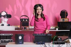 leende konstnär stående på dj tabell spelar techno musik på professionell mixer trösta i studio över rosa bakgrund. asiatisk musiker utför elektronisk ljud, har roligt i klubb på natt tid foto