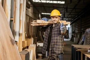 smart manlig konstruktion arbetstagare arbete bära trä- lugg i möbel fabrik stående tummen upp leende. foto
