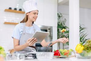 skön modell Lycklig kvinna friska mat matlagning vegetabiliska sallad i kök med uppkopplad läsplatta foto