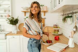 Söt flicka ser på recept i kokkonst bok framställning vegetabiliska sallad matlagning mat i ljus kök på Hem. bantning friska livsstil begrepp. foto