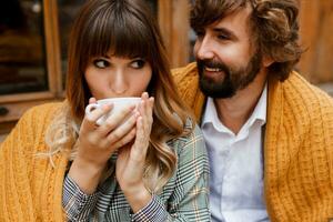 stänga upp mysigt värma porträtt av Lycklig kramas par i kärlek. stilig man och Söt kvinna har frukost och dricka kaffe på terrass. foto