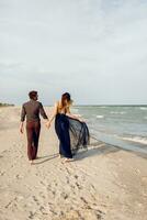 se från tillbaka. elegant par i kärlek gående längs de strand. romantisk ögonblick. vit sand och hav vågor. tropisk semester. full höjd. foto