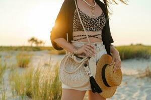 mode detaljer.kvinna i eleganta boho sommar ha på sig gående på de strand. värma solnedgång färger.halm hatt. foto