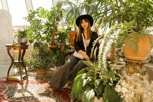 elegant självsäker kvinna i tillfällig utrusta Framställ i Hem trädgård. tropisk växter, bohemisk interiör. foto