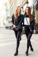 två eleganta Söt flickor Framställ på de gata i solig dag. bär trendig urban utrusta , läder jacka och stövlar hälar. foto