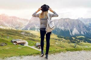 kvinna resande hipster med ryggsäck innehav hatt och ser framåt- på Fantastisk bergen och dal se. Plats för text. bär eleganta boho falla utrusta. foto