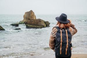 kvinna i hatt och med ryggsäck på stranden på en bakgrund av havet