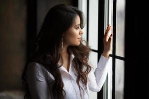 vacker mörkhårig ung kvinna tittar ut genom fönstret foto
