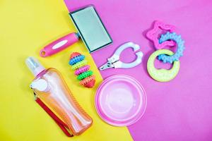 husdjurstillbehör koncept - skål, leksaker, borste, halsband och nagelsax på gul och rosa bakgrund. foto