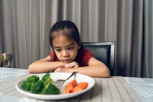 liten söt unge flicka vägrar till äta friska grönsaker. barn do inte tycka om till äta grönsaker. foto