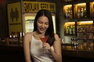 asiatisk kvinna dricker en cocktail på en bar på natten. foto