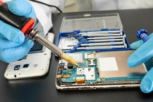 tekniker som reparerar insidan av mobiltelefonen med lödkolv. foto